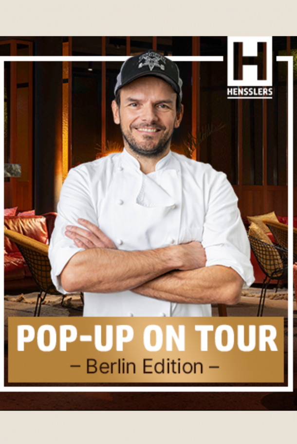 A smiling chef in a white uniform stands with arms crossed in front of restaurant seating; text reads Pop-Up On Tour - Berlin Edition.