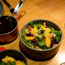 Eine Schüssel Feldsalat mit frischem Grün und Orangenscheiben, begleitet von einem silbernen Löffel.