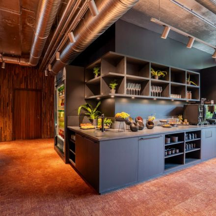 Modern kitchen with open shelves, plants, and various dishes on a counter, featuring industrial ceiling and warm lighting.