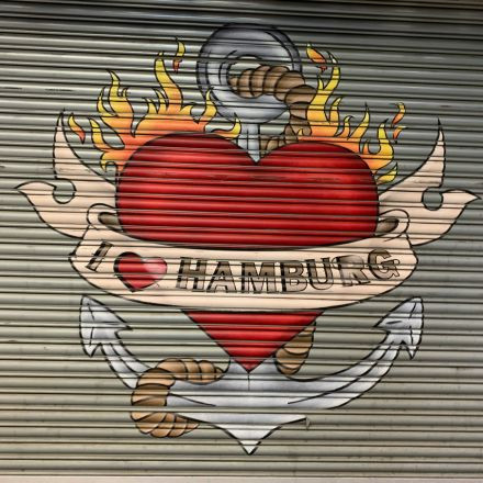 Graffiti eines flammend roten Herzens mit einem Anker und einem Banner mit der Aufschrift „I ♥ HAMBURG“ auf einem Metallrollladen.