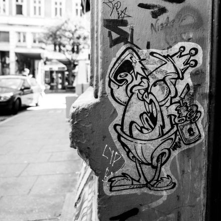 Schwarzweißfoto eines Graffiti-Cartoon-Vogels mit Krone und Flasche, der mit anderer Straßenkunst und Graffiti an eine Wand geklebt ist.