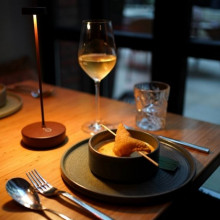  Ein schummrig beleuchteter Restauranttisch, gedeckt mit Besteck, einer Schüssel Suppe mit Gebäck, einem Weinglas und einem Glas Wasser.