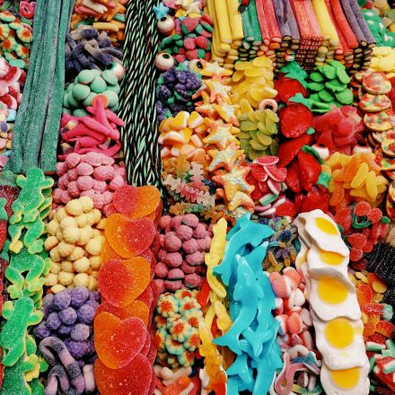 Verschiedene bunte Süßigkeiten, darunter Gummibärchen, Herzen, Eier und Seile, in hellen, geordneten Reihen angeordnet.