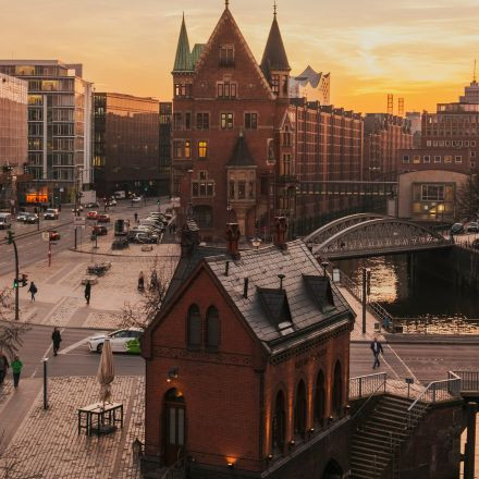 Ein Blick auf historische Backsteingebäude bei Sonnenuntergang an einem Kanal in einer Stadt, mit Menschen und Autos auf den umliegenden Straßen.