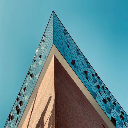 Ein modernes Gebäude mit einer Außenfassade aus Backstein und Glas, von unten vor einem klaren blauen Himmel fotografiert.
