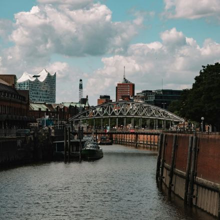 Ein Kanal mit einer Brücke darüber, gesäumt von Backsteingebäuden, unter einem teilweise bewölkten Himmel in einer städtischen Stadtlandschaft.