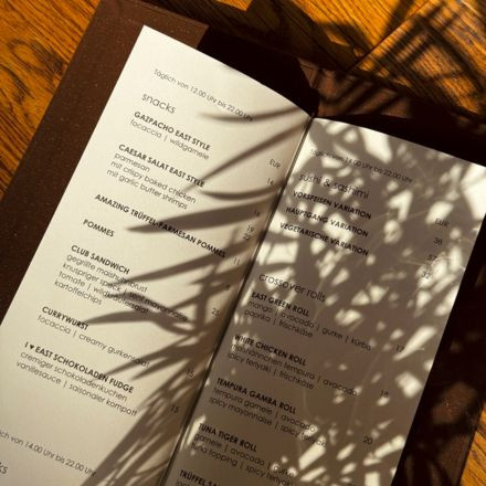 A restaurant menu on a table, partially shaded by leafy shadows, with sunlight highlighting some of the text.