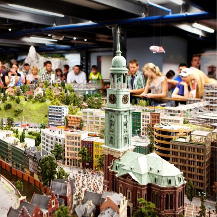 In einer Innenausstellung können die Besucher eine detaillierte Miniaturstadtdarstellung mit farbenfrohen Gebäuden, einer Kirche und einem zentralen Uhrenturm beobachten.