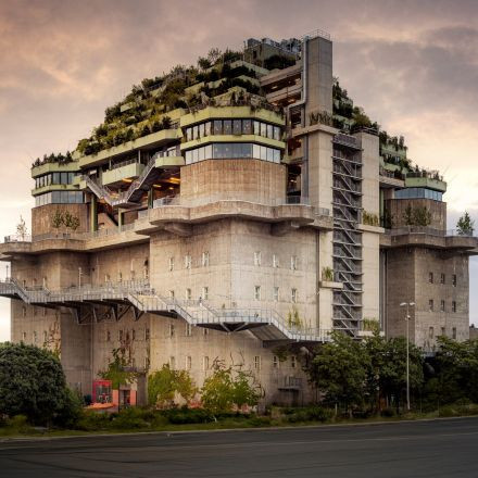 Ein großes Betongebäude mit mehreren Terrassen, die mit Grün und Pflanzen bedeckt sind und bei Sonnenuntergang an einen modernen Stadtgarten erinnern.