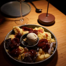 Eine Schüssel mit fluffigem Kaiserschmarrn, garniert mit Eis, steht auf dem Tisch neben einem Glas Rotwein.