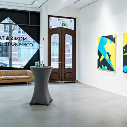 Moderne Kunstgalerie mit hellen abstrakten Gemälden an weißen Wänden, einem braunen Sofa und einem hohen gedeckten Tisch neben großen Glastüren.