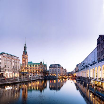 Ein Kanal in einer Stadt in der Abenddämmerung, mit historischen Gebäuden und einem Uhrturm, die sich im ruhigen Wasser spiegeln.