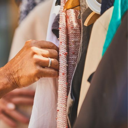 A hand with a ring searches through clothes hanging on wooden hangers on a rack.