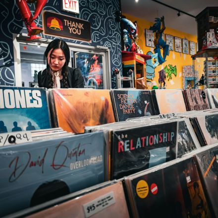 A person browses for records in a colorful music store whose walls are decorated with posters, toys, and artwork.
