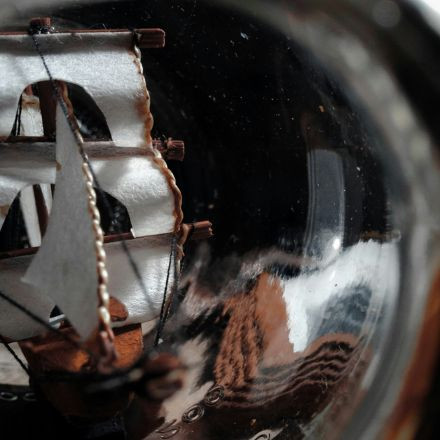 Close-up of a ship model with white sails in a glass bottle, seen from the bottle opening.