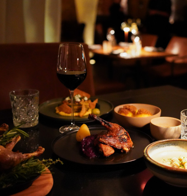 Ein schwach beleuchteter Restauranttisch mit Wein, Wasser, gebratener Ente, Hühnchen und verschiedenen Beilagen für das Abendessen.