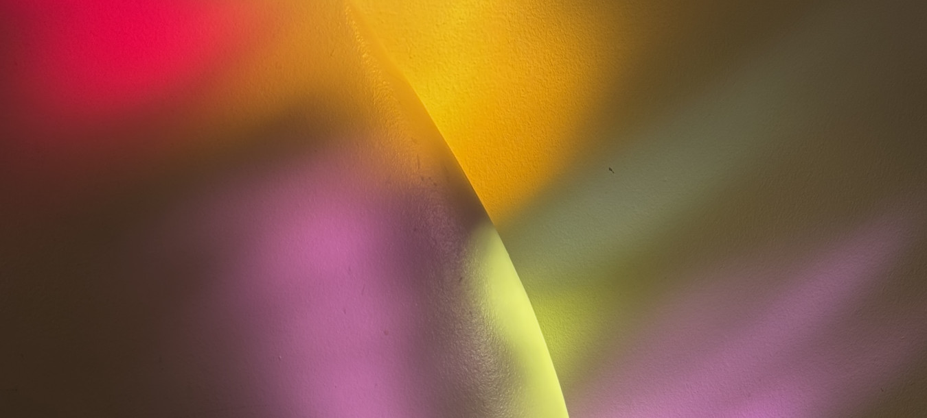 Colorful light reflections—yellow, pink, and purple—cast on a curved white wall and dark wooden floor.