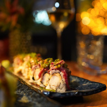 Sushi-Rolle auf einem Teller neben einem Glas Weißwein, elegant angerichtet für ein gehobenes Speiseerlebnis.
