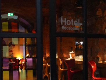 A welcoming hotel reception area with colorful chairs, warm lighting, and glass doors that reflect the interior light.