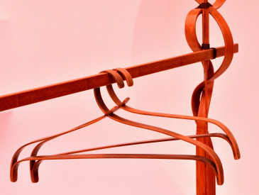 Two wooden coat hangers on a wooden coat rack, against a pink background with soft lighting.