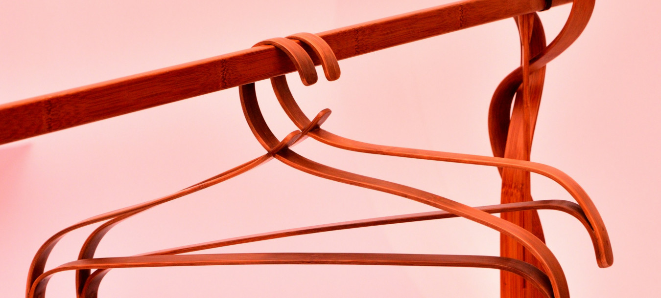 Two wooden coat hangers on a wooden coat rack against a pink background with soft lighting.