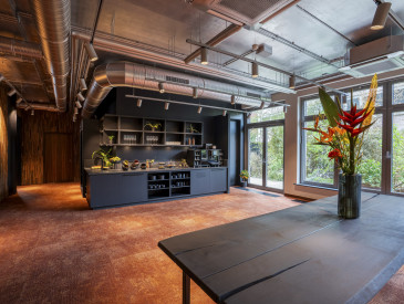 Modern kitchen with exposed pipes, large windows, dark cabinets, and a table with a tropical flower arrangement.