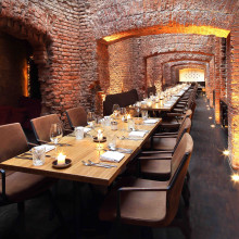 Ein Restaurantinterieur mit einer rustikalen Backsteinwand und einem langen Holztisch, der zum Essen gedeckt ist.