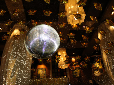 A shimmering disco ball reflects light in a festive room adorned with numerous gold star-shaped balloons and elegant chandeliers, creating a celebratory ambiance.