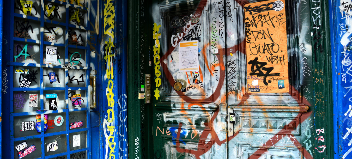 Blaue Wand und grüne Tür bedeckt mit bunten Graffiti, Tags und Aufklebern in einem städtischen Umfeld.