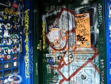 Eine Doppeltür und eine nahe gelegene Wand sind mit bunten Graffiti, Aufklebern und Tags in verschiedenen Stilen und Farben bedeckt.